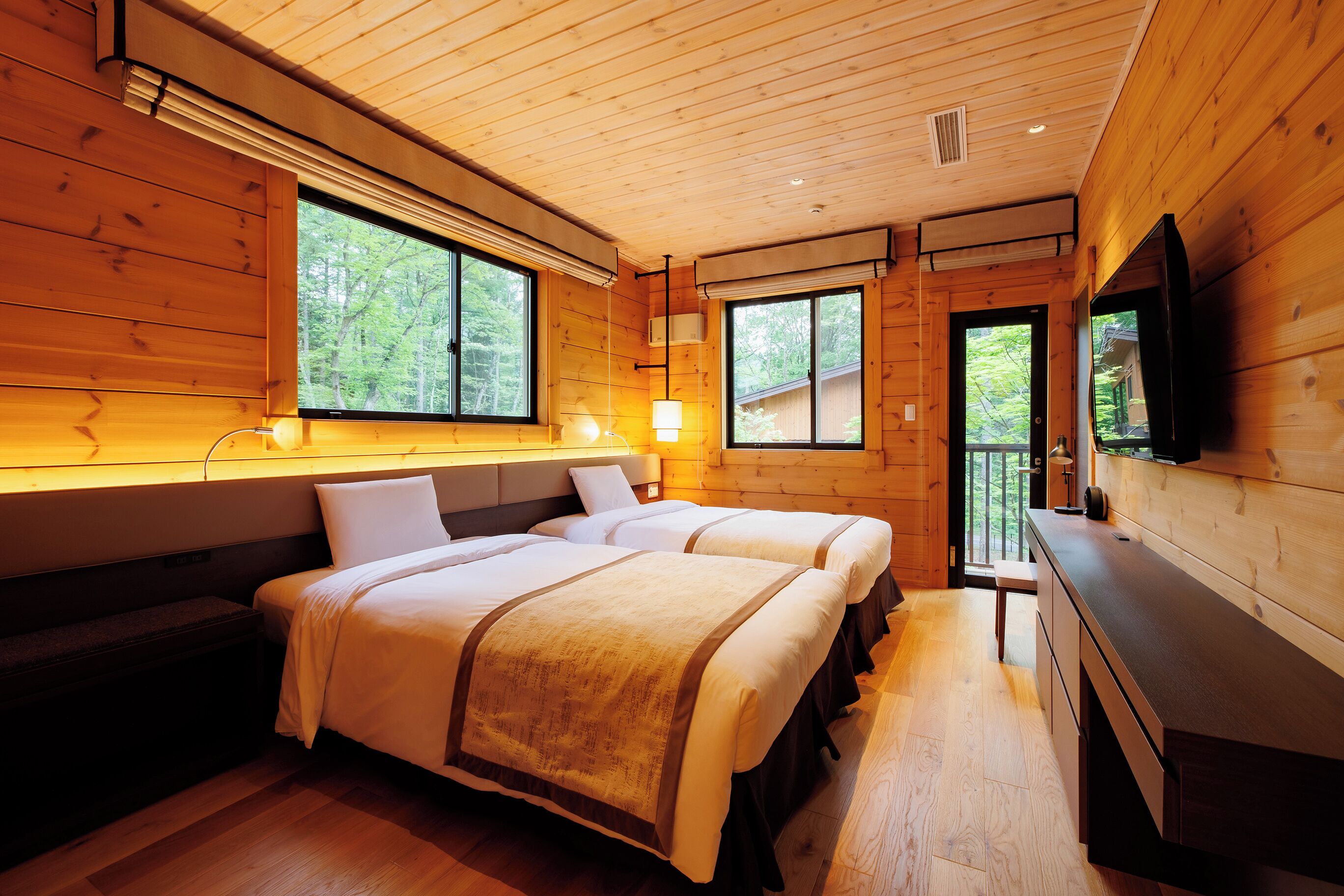 A wooden cabin room with two beds, a bench, a desk, and a TV.