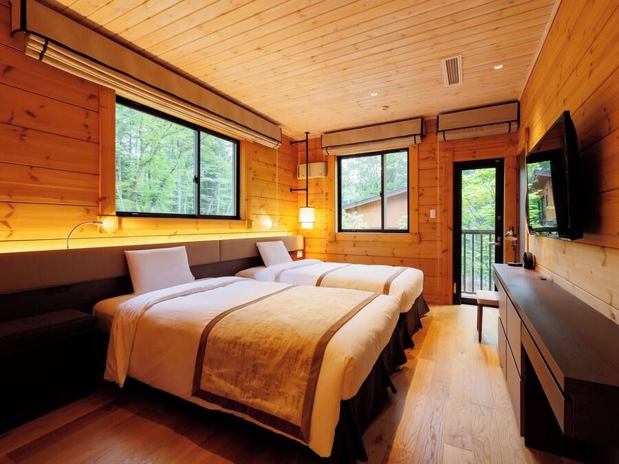 A wooden cabin room with two beds, a bench, a desk, and a TV.
