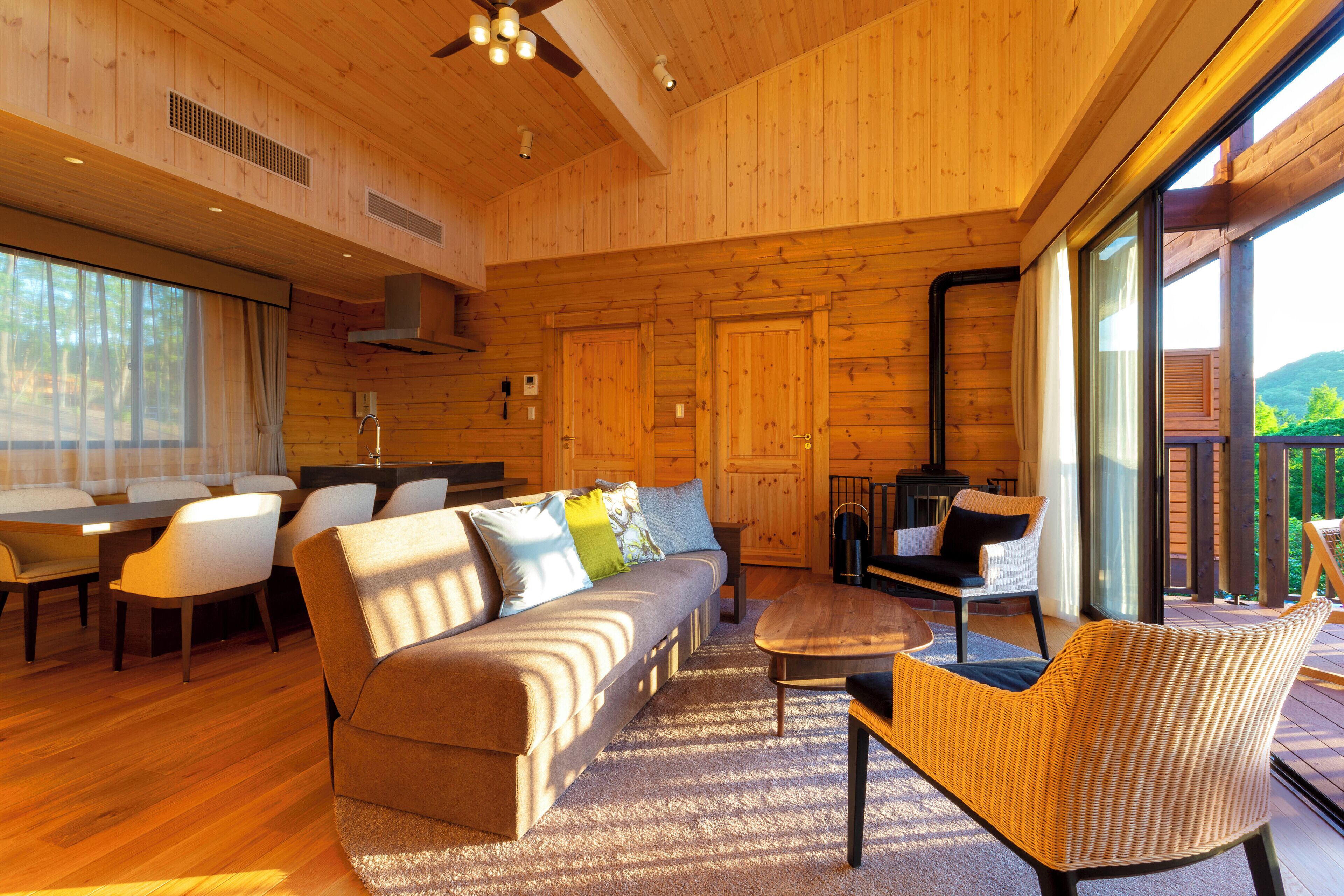 Interior moderno de cabaña de troncos con piso de madera, un sofá, sillas, una mesa de comedor y un ventanal con vistas al exterior.
