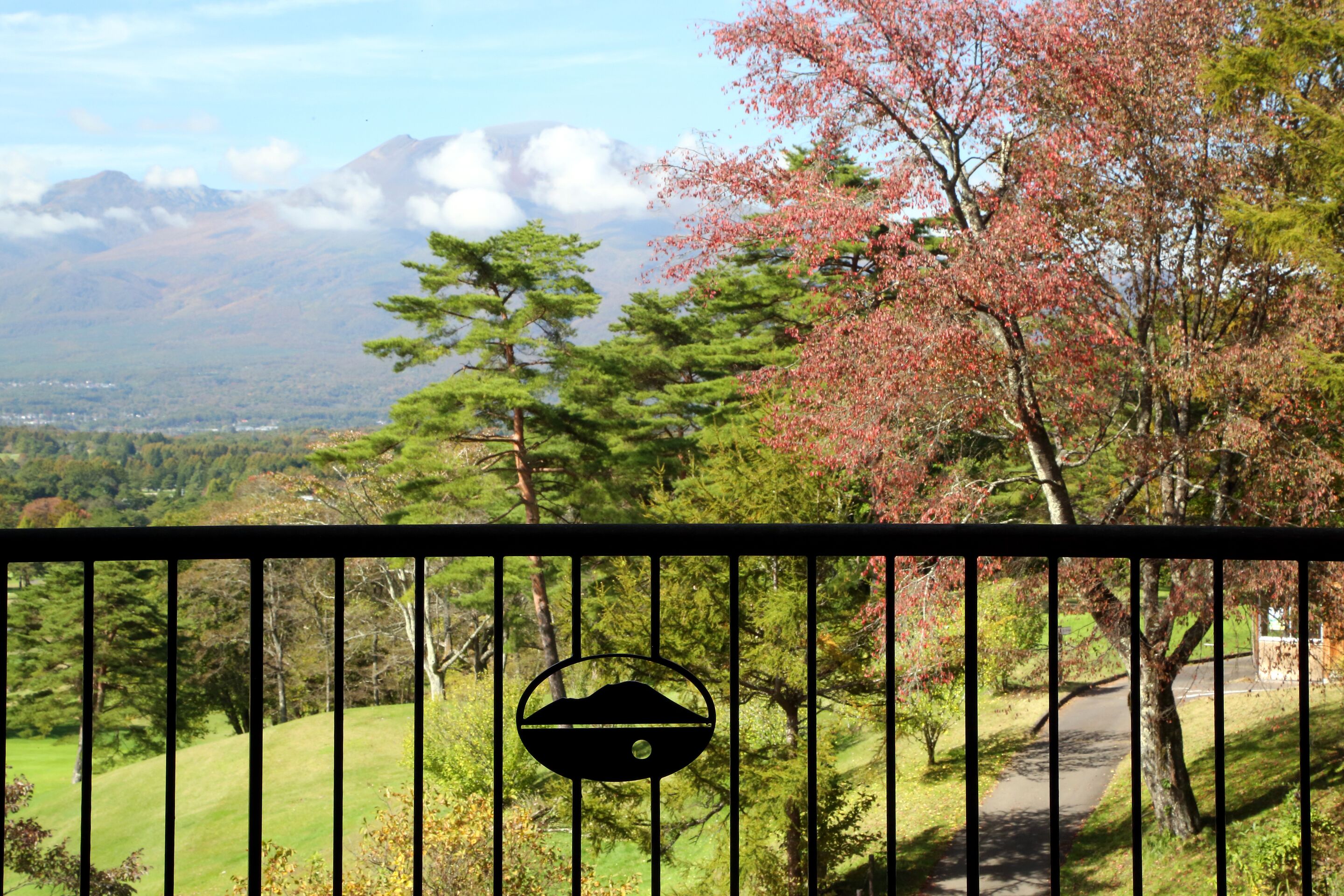 A scenic view of a mountainous landscape with a pathway and a fence with a circular emblem.