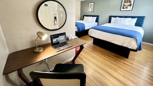 A hotel room with a desk, laptop, two beds, and a round mirror. - Ashland Motel - Oregon (Ashland)