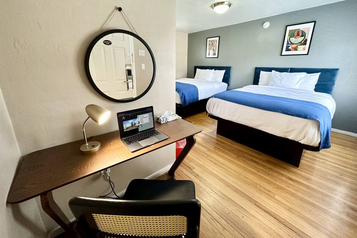 Une chambre d’hôtel équipée d’un bureau, d’un ordinateur portable, de deux lits et d’un miroir rond.