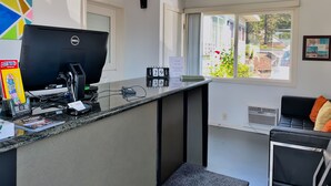 A hotel reception area with a Dell computer, a calendar, and a window with a view of the outside. - Ashland Motel - Oregon (Ashland)