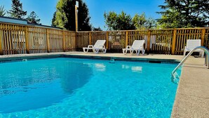 A clear swimming pool with a wooden fence, surrounded by lounge chairs. - Ashland Motel - Oregon (Ashland)