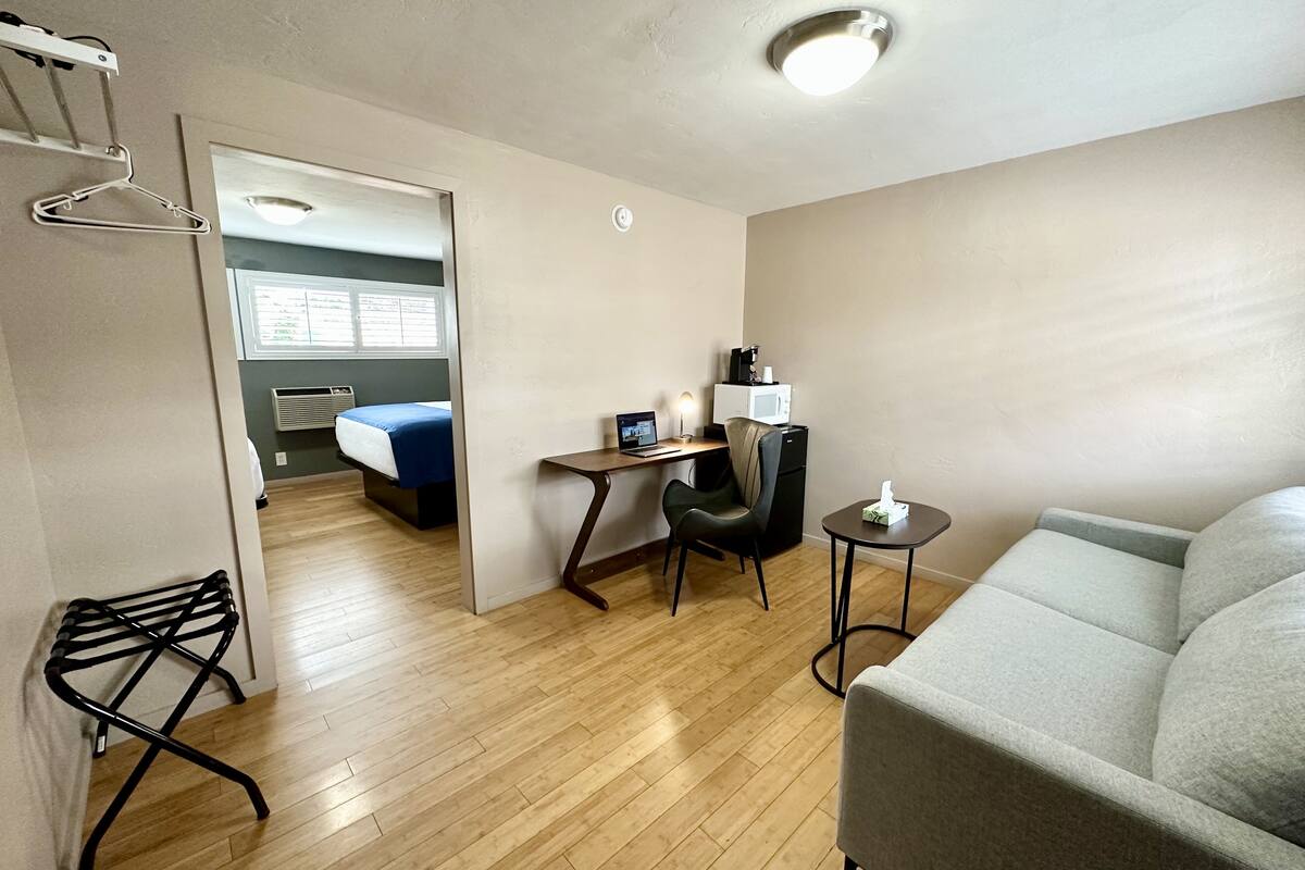 Une chambre d’hôtel moderne équipée d’un lit, d’un bureau avec un ordinateur, d’une chaise, d’une petite table et d’un canapé.