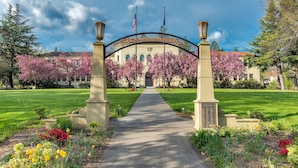 A pathway leading to a building with a decorative archway, surrounded by flowering trees and a well-maintained lawn. - Ashland Motel - Oregon (Ashland)