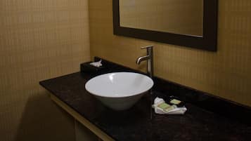 A bathroom with a white sink, dark countertop, and a mirror with a light above it.