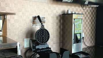 A kitchen area with a waffle maker, a coffee machine, and a beverage dispenser.