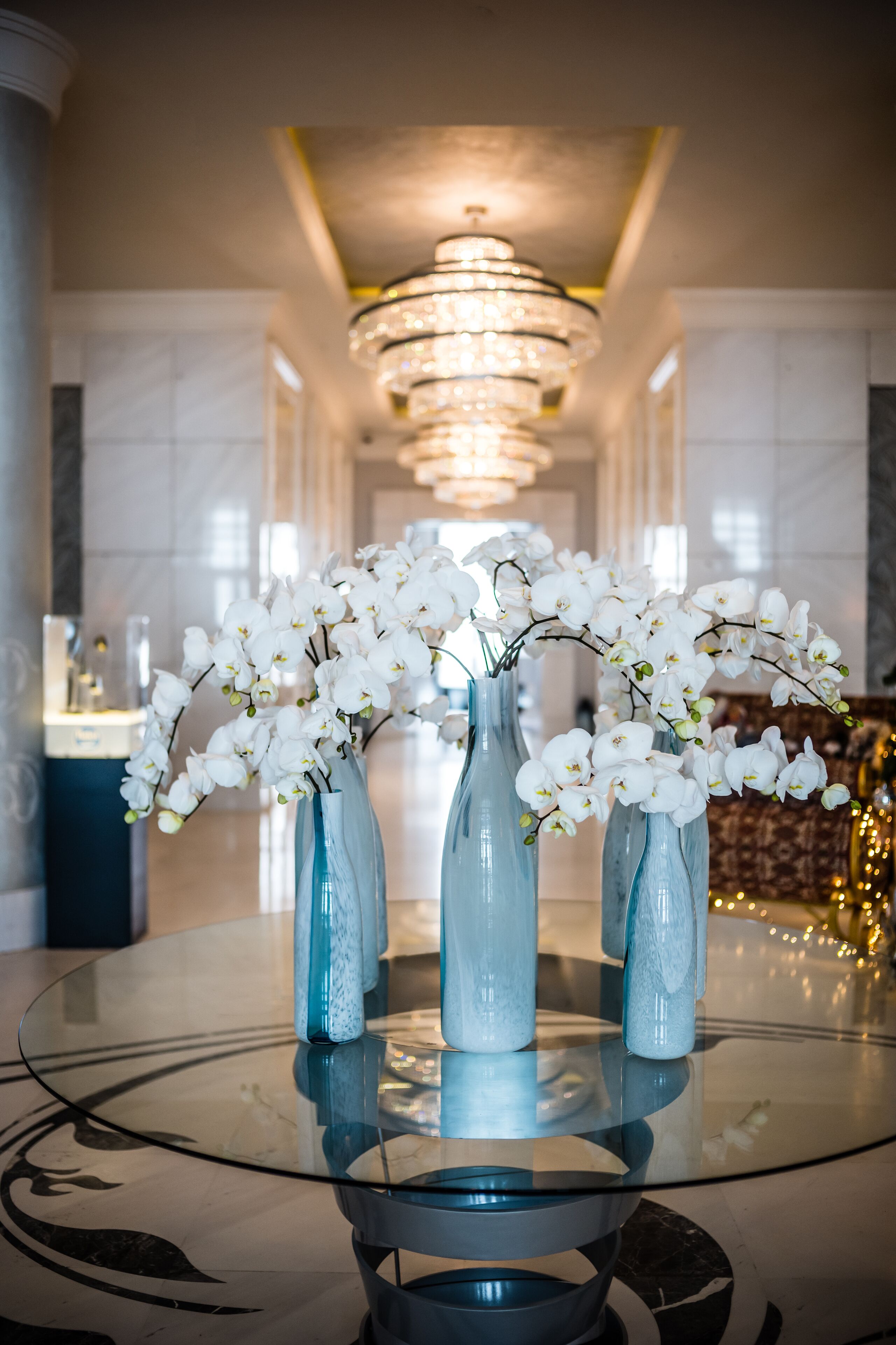Una mesa de vidrio con tres jarrones de orquídeas blancas.