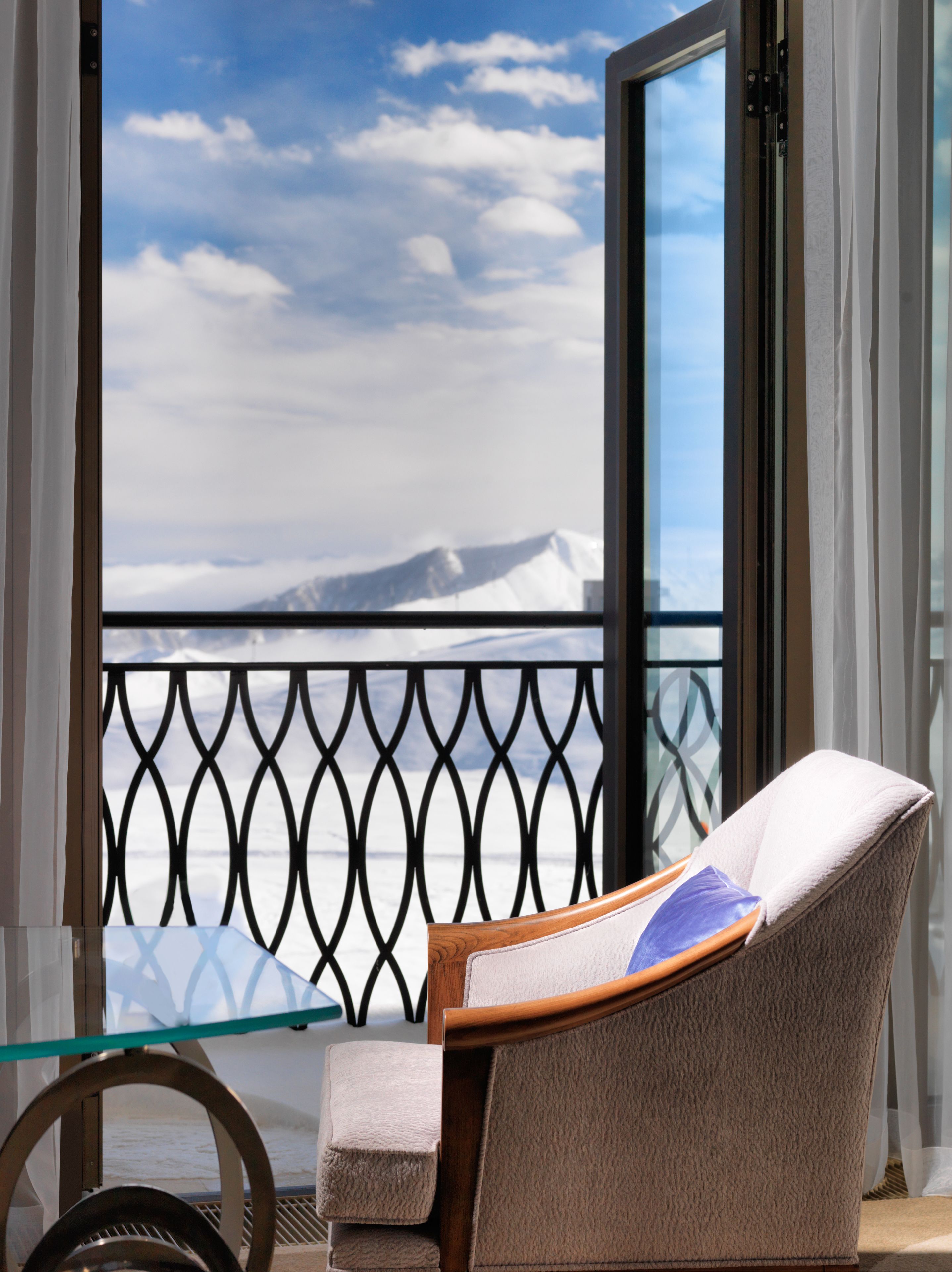 A chair with a cushion and a glass table in front of a balcony with a metal railing.
