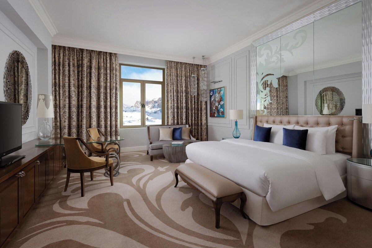 Habitación de hotel con una cama grande, televisión, escritorio con lámpara, una silla y un sofá.