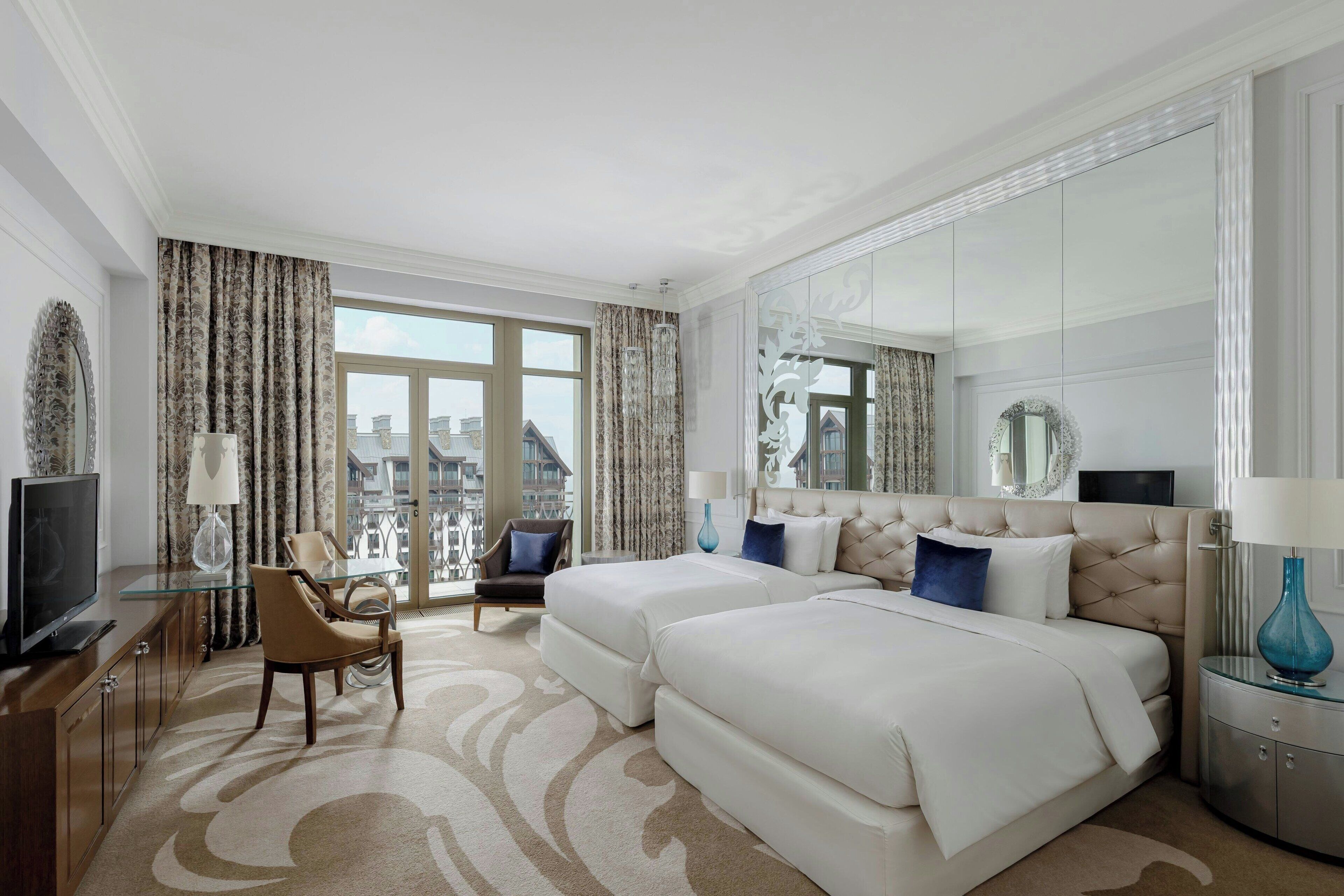 A hotel room with a large bed, a TV, a chair, a desk, and a view of the city.