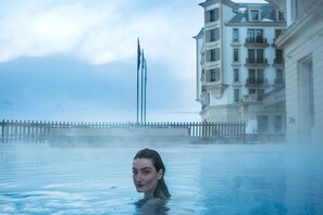 A person in a large indoor pool with a view of a building and a wooden fence in the background.