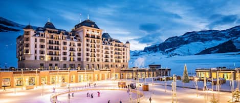 A hotel with a large central building, multiple balconies, and a snow-covered landscape with mountains in the background.