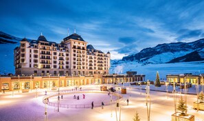 A hotel with a large central building, multiple balconies, and a snow-covered landscape with mountains in the background.