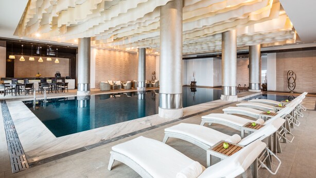 A modern indoor pool area with lounge chairs, a coffee station, and a brick wall. - Pik Palace, Shahdag, Autograph Collection (Qusar)