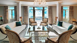 A spacious living room with a large chandelier, two sofas with cushions, a glass coffee table, and a view of a snowy landscape through large windows. - Pik Palace, Shahdag, Autograph Collection (Qusar)