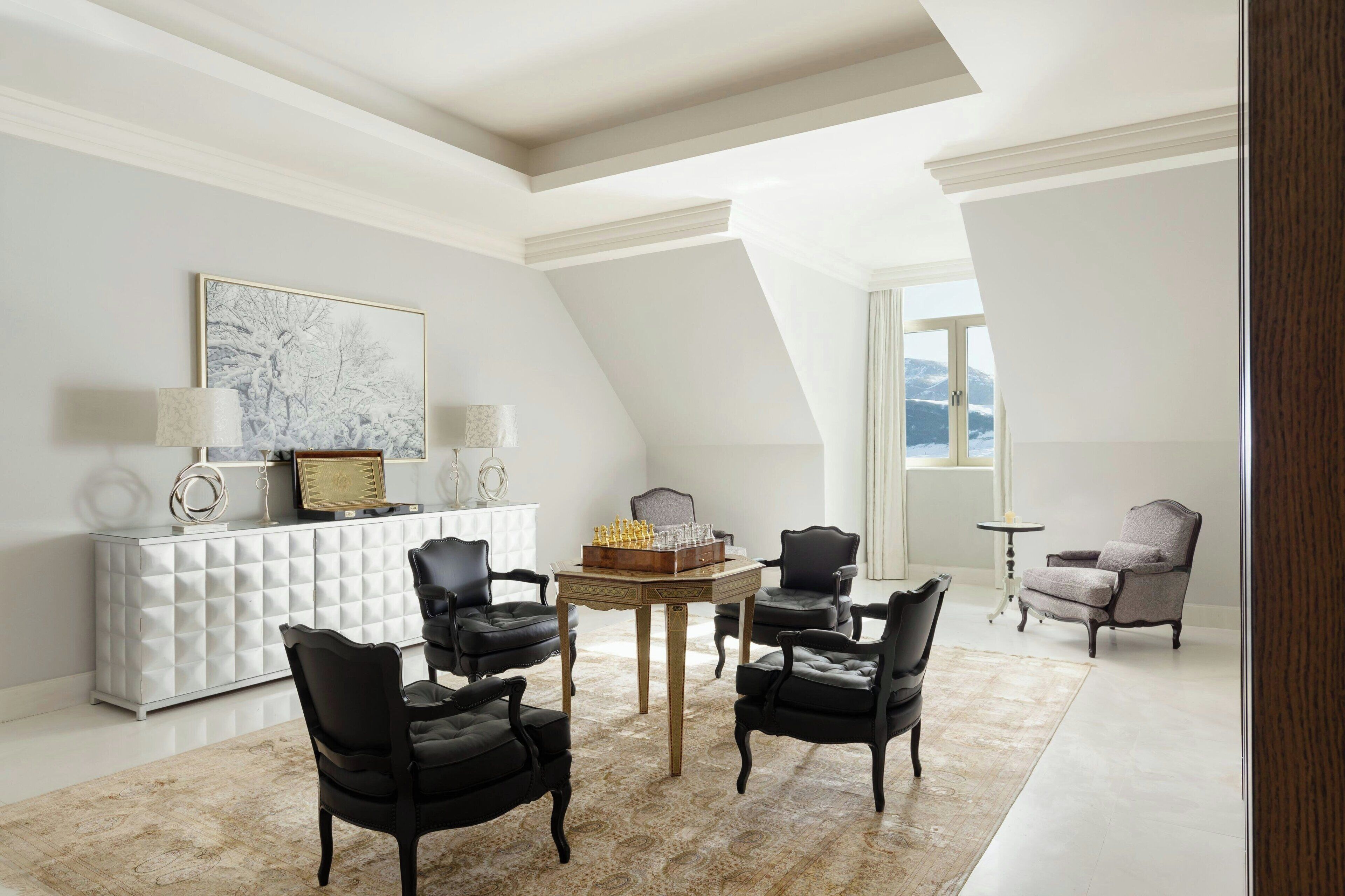 A modern living room with a white console, a chess table, and four black chairs.