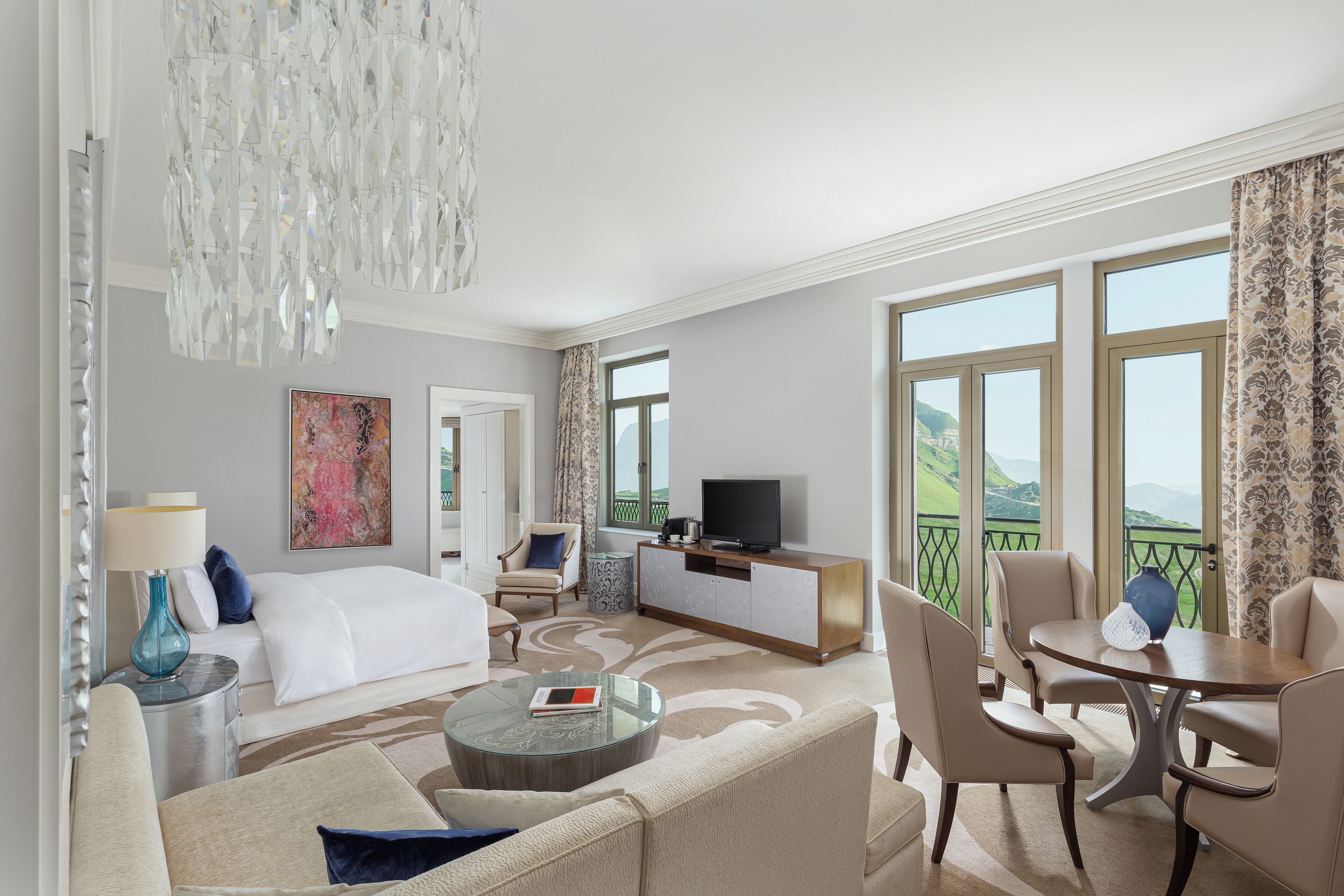 A hotel room with a bed, a sofa, a coffee table, a TV, and a balcony with a view.
