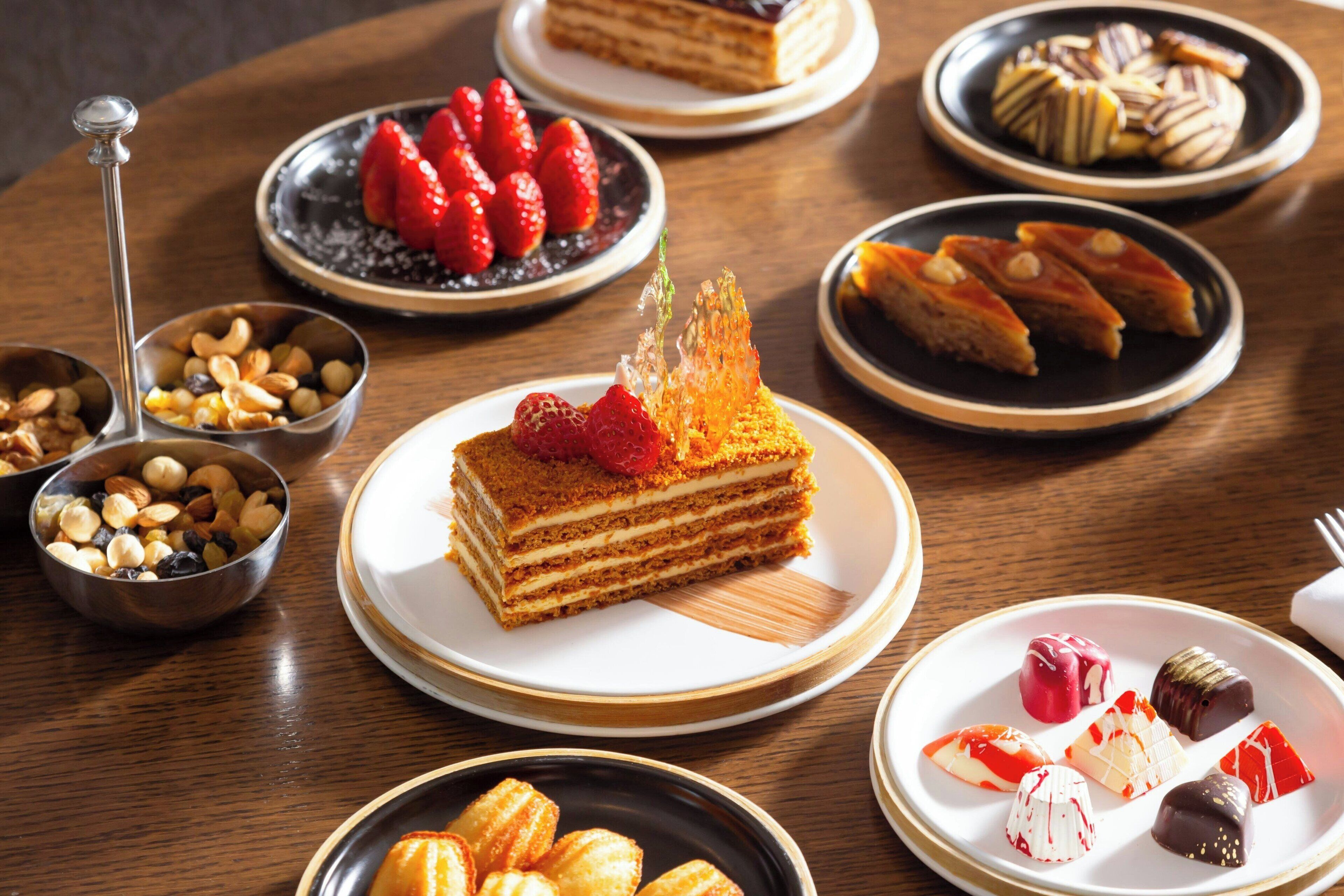 A variety of desserts on plates, including a layered cake with strawberries and a chocolate dessert with nuts.