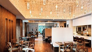 A restaurant with wooden flooring, wooden chairs, and tables. There is a kitchen area with a chef preparing food. - Pik Palace, Shahdag, Autograph Collection (Qusar)