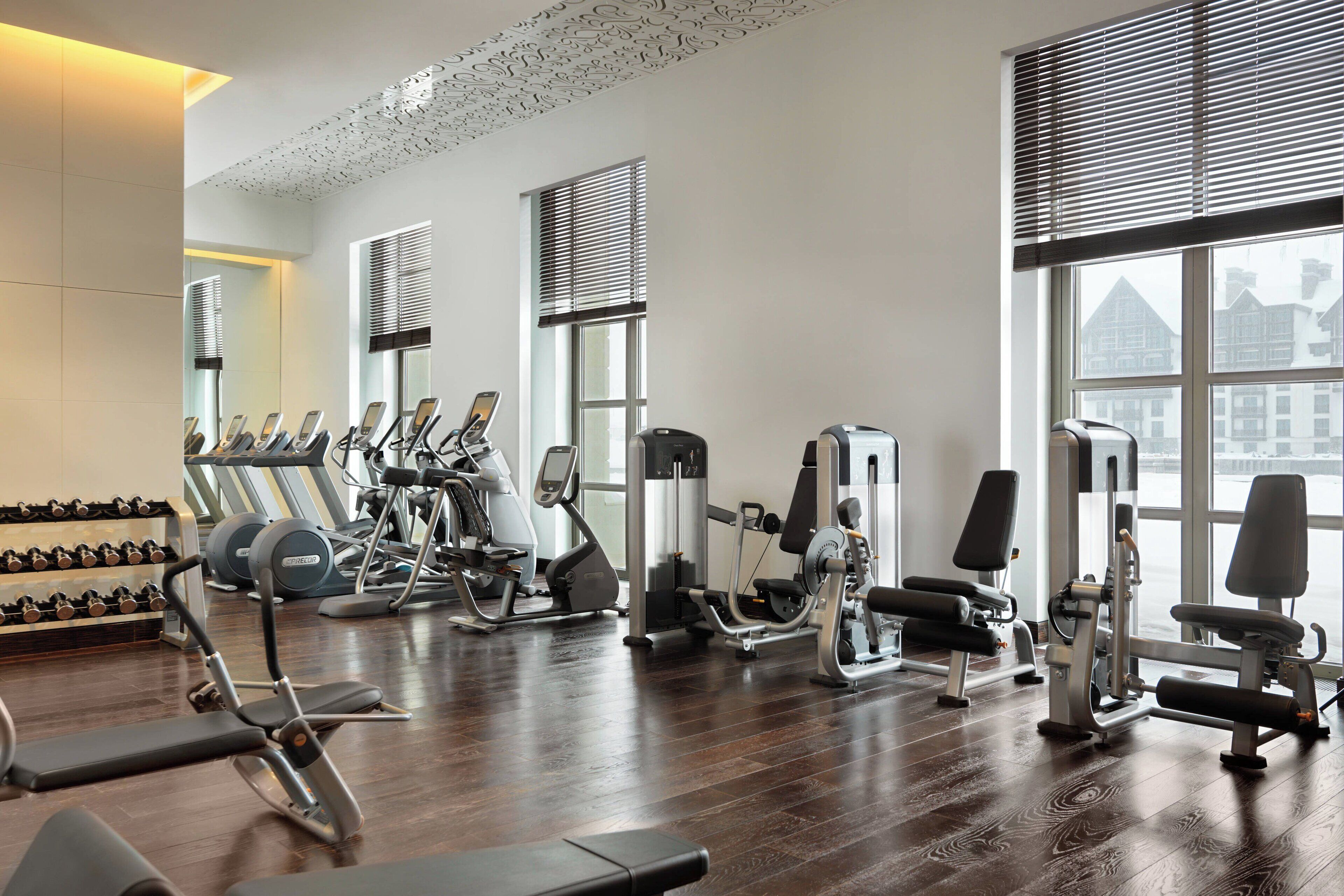A gym with various exercise equipment, large windows, and a wooden floor.