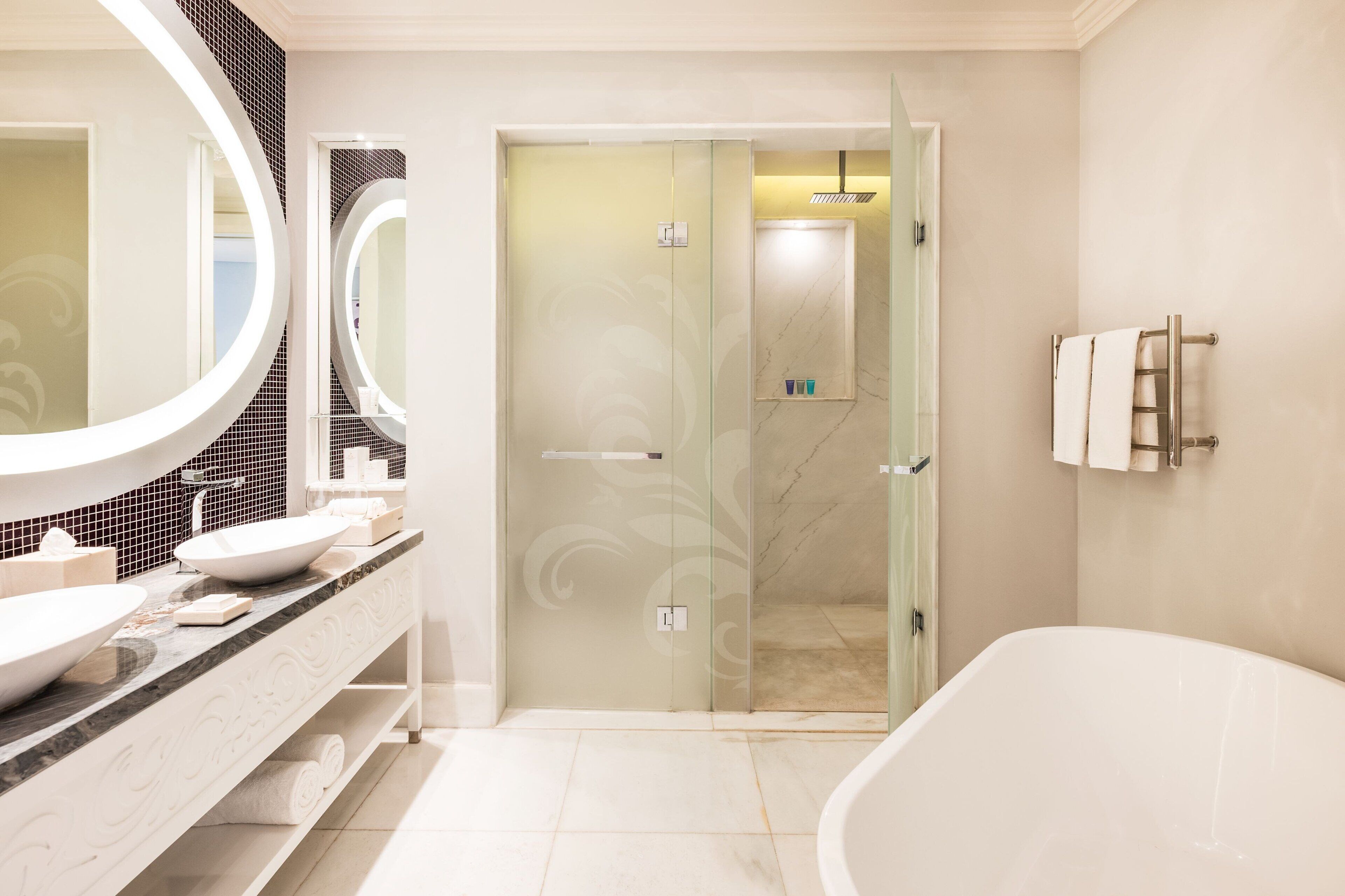 A modern bathroom with a large mirror, two sinks, a bathtub, and a shower area.