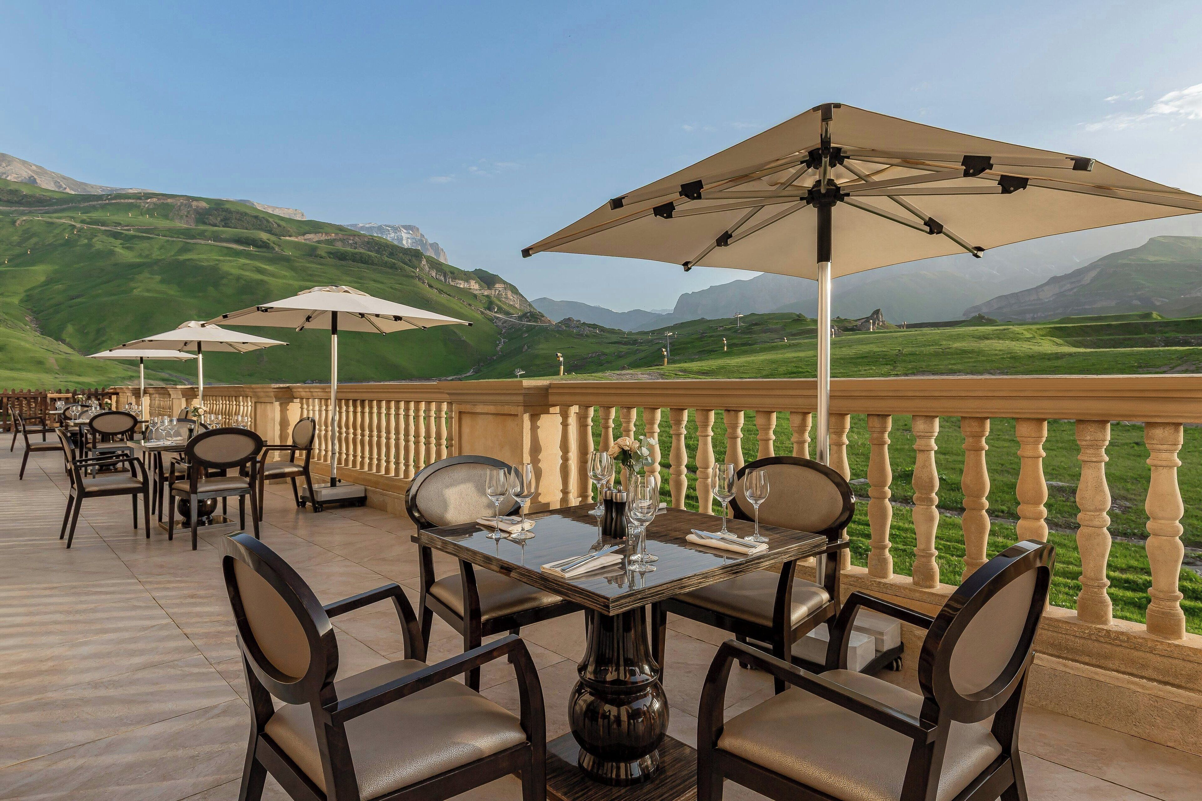 An outdoor dining area with tables and chairs, umbrellas, and a scenic mountain view.