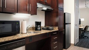 A compact kitchen with dark wood cabinets, a built-in microwave, a coffee maker, and a refrigerator. - TownePlace Suites by Marriott Laredo (Laredo)