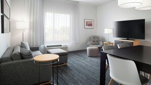 A modern hotel room with a grey sofa, a round table, a flat-screen TV, and a large window with white curtains. - TownePlace Suites by Marriott Laredo (Laredo)
