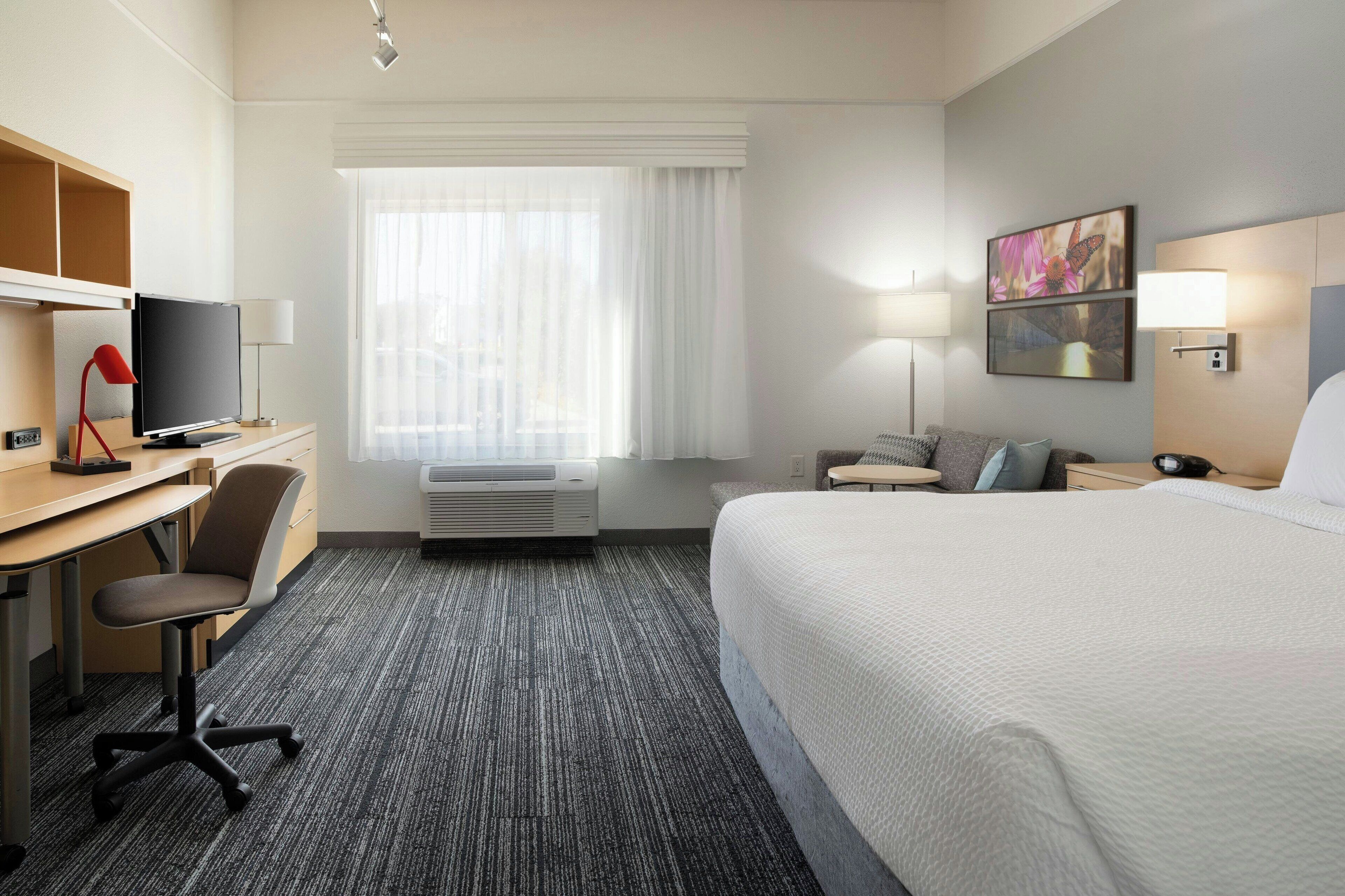 A hotel room with a bed, desk, chair, television, and a window with curtains.