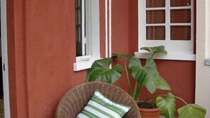 A wicker chair with a teal cushion outside a building with red walls and white trim. - Adam Suites (Santo Domingo)