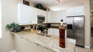 A kitchen with white cabinets, a stainless steel refrigerator, a microwave, and a granite countertop.