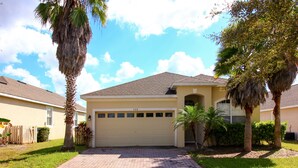 A single-story house with a garage, surrounded by palm trees and a brick driveway.