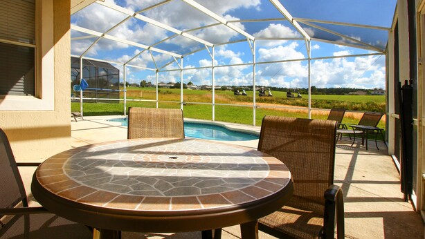 A covered patio with a round table and chairs, a pool, and a view of a golf course.