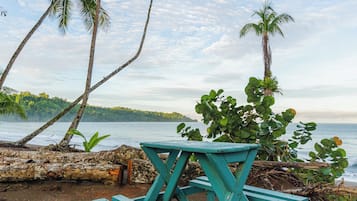 A picnic table on a sandy beach with palm trees and a view of the water.
