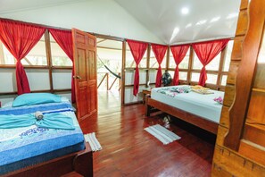 A room with two beds, wooden flooring, and red curtains. - Poor Man's Paradise (Drake Bay)
