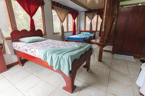 A bedroom with a wooden bed, a small bedside table, and a window with curtains. - Poor Man's Paradise (Drake Bay)
