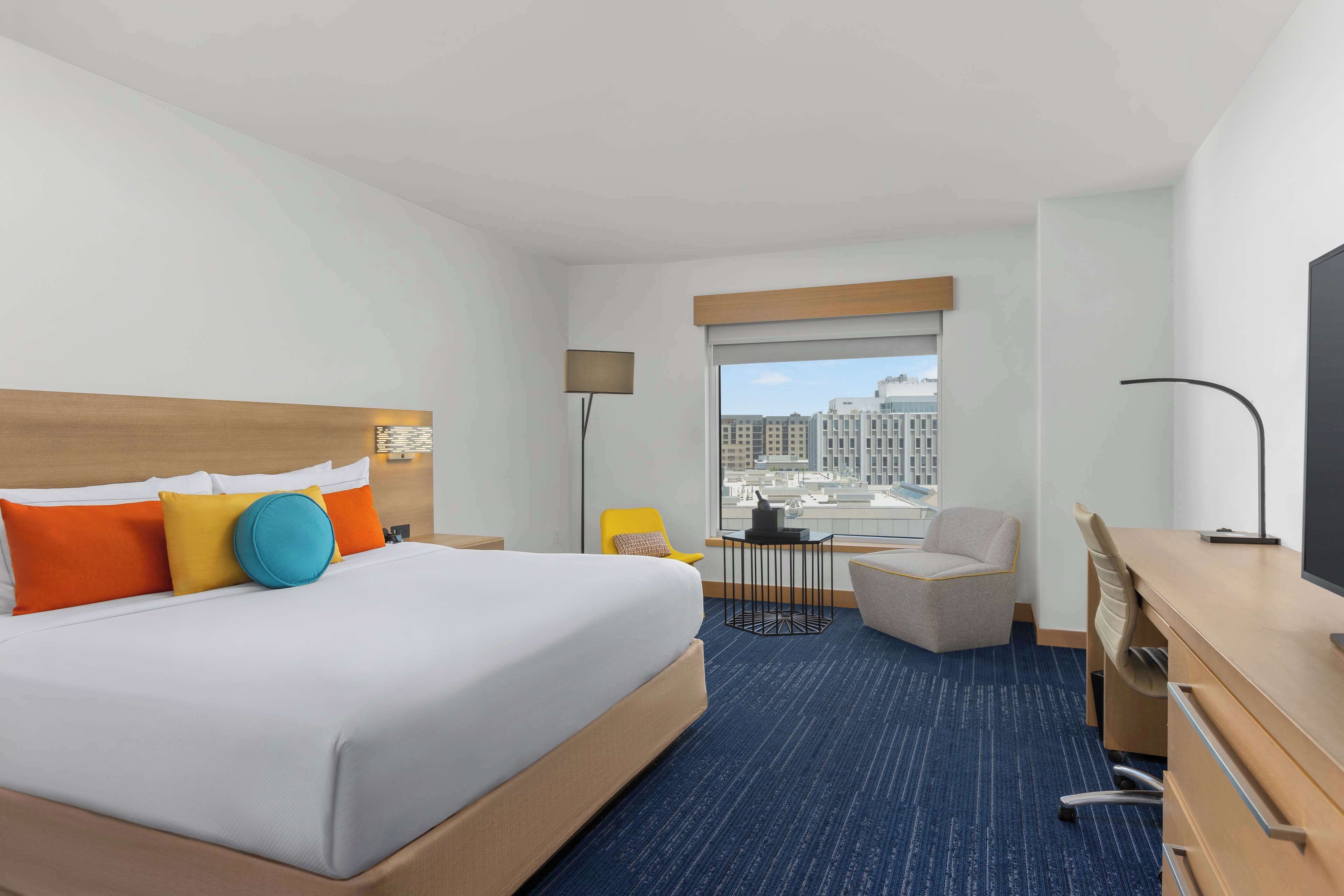 Een hotelkamer met een groot bed, een bureau, een stoel en een uitzicht op de stad door het raam.