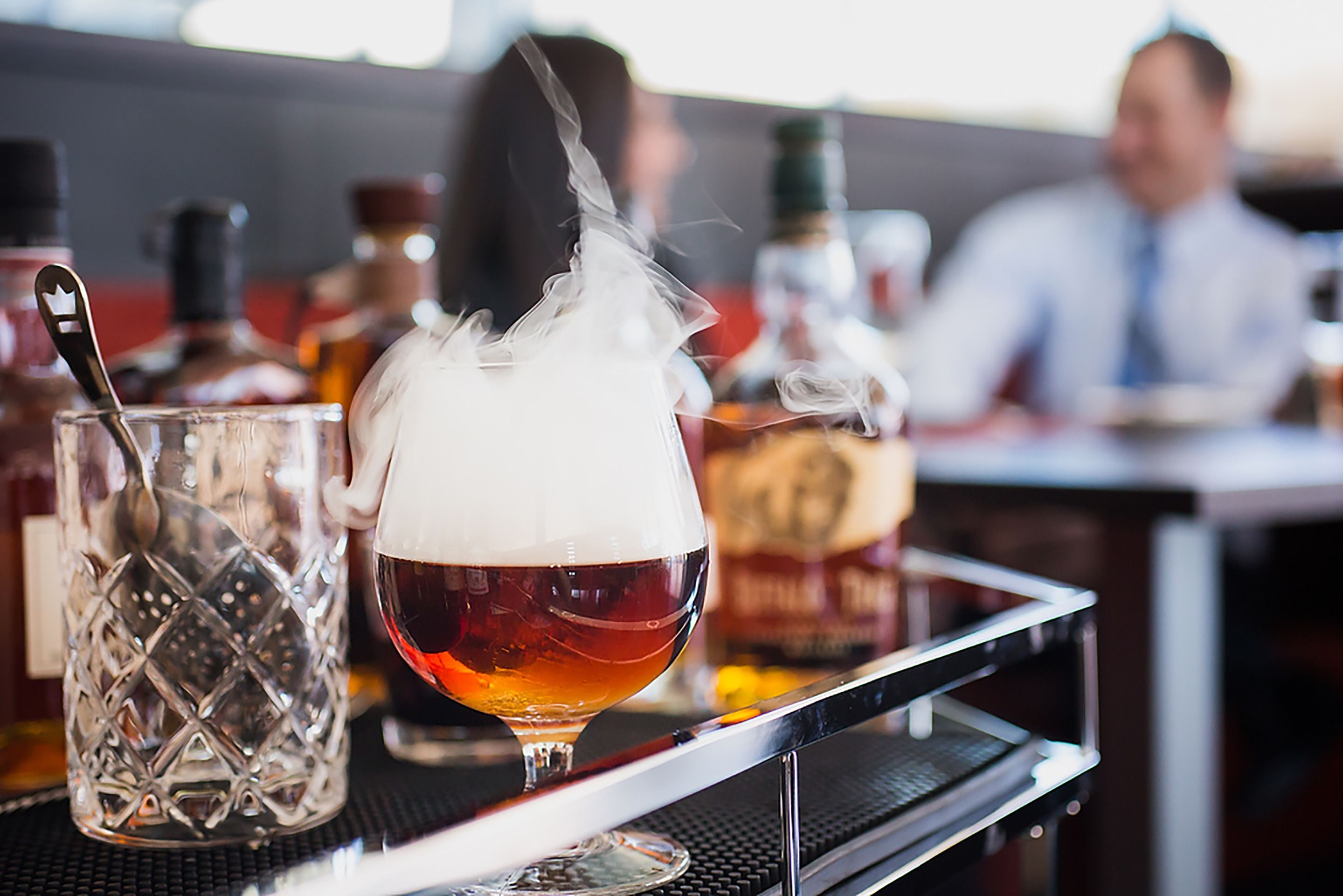 A bar setting with a glass of beer and a bottle of whiskey on a tray.