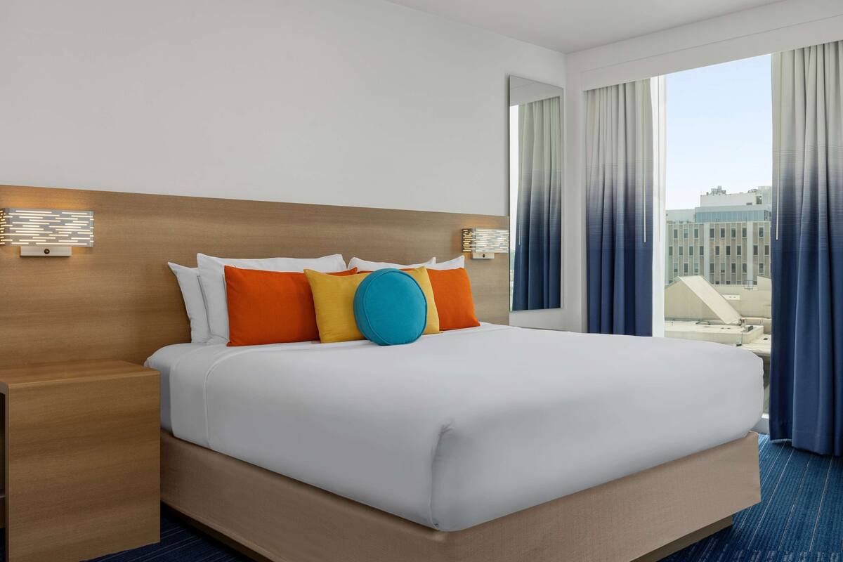 A hotel room with a large bed, a wooden headboard, and a view of buildings through the window.