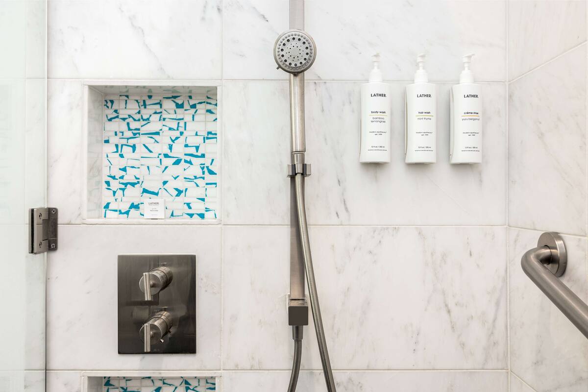 A modern bathroom with a shower, a handheld showerhead, and three bottles of Lather body wash.