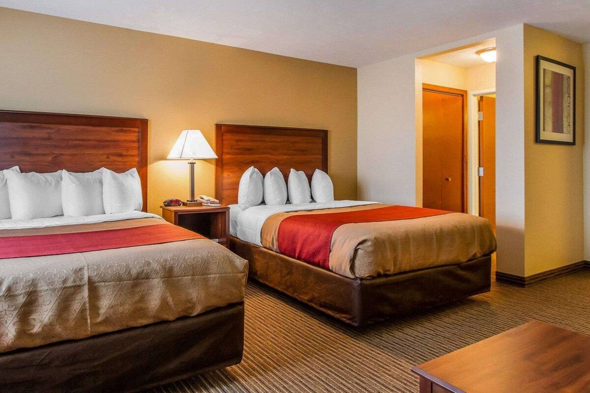 A hotel room with two beds, a nightstand with a lamp, and a door leading to another room.