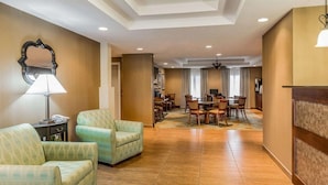 Eine Hotelhalle mit einer Rezeption, zwei Sesseln, einem Essbereich mit einer Chandelüster und einem gemusterten Teppich.