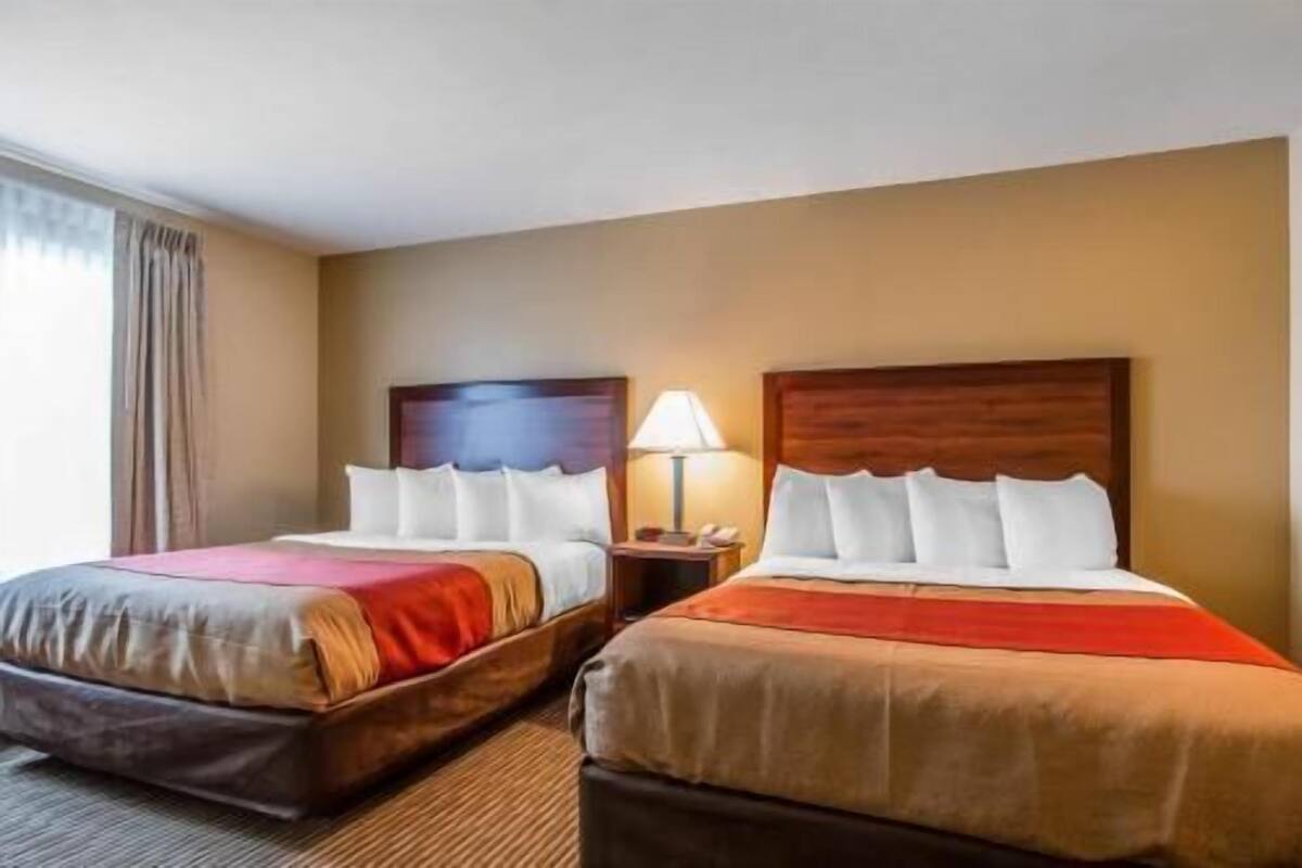 A hotel room with two beds, a nightstand with a lamp, and a window with curtains.