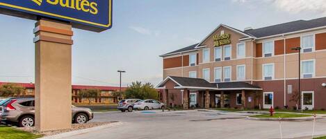 A MainStay Suites hotel with a clear sign, a parking lot, and a building with a brown facade and multiple windows.