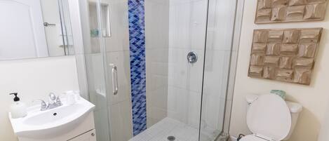 A bathroom with a glass-enclosed shower, a white sink with a marble countertop, and a toilet.