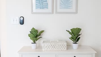 A white dresser with two potted plants, a white box, and four framed leaf designs on the wall.