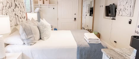 Un dormitorio ordenado con cama, mesita de noche y televisor instalado en la pared.