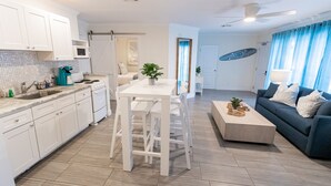 A modern kitchen with white cabinets, a dining area with a white table and chairs, a blue sofa with white cushions, and a ceiling fan. - Siesta Key Beachside Villas (Siesta Key)